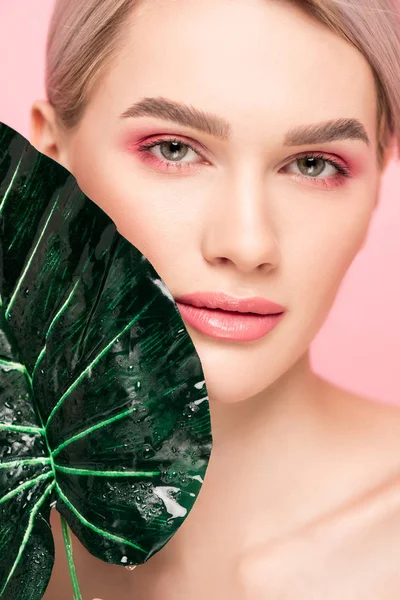 Hermosa chica con maquillaje rosa aislado en rosa con hoja verde - foto de stock