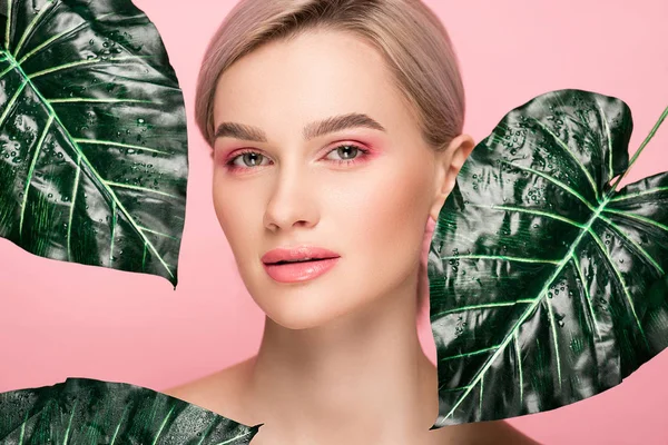 Attractive girl with pink makeup isolated on pink with green leaves — Stock Photo