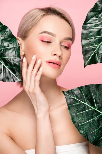 Menina atraente com maquiagem rosa isolado em rosa com folhas verdes — Fotografia de Stock