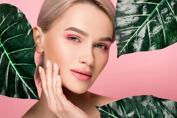 Attraktive zarte Mädchen mit rosa Make-up isoliert auf rosa mit grünen Blättern — Stockfoto