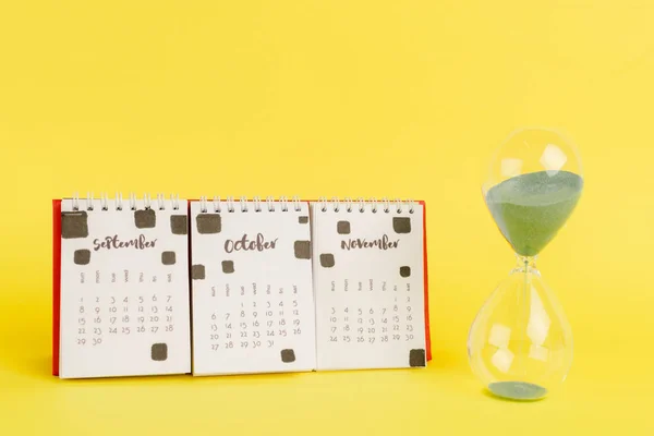 Ampulheta perto do calendário com bocas de outono no fundo amarelo — Fotografia de Stock