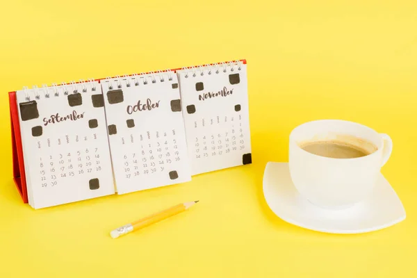 Cup of coffee near calendar and pencil on yellow background — Stock Photo