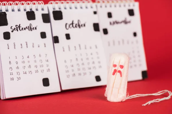 Concentration sélective du tampon hygiénique avec expression triste du visage près du calendrier sur fond rouge — Photo de stock