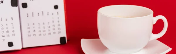 Panorâmica tiro de xícara de café e calendário em fundo vermelho — Fotografia de Stock