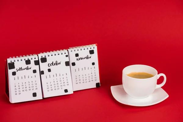 Calendario con meses de otoño y taza de café sobre fondo rojo - foto de stock