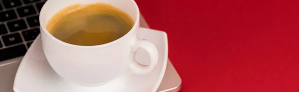 Крупним планом кавова чашка на ноутбуці на червоному тлі, панорамний знімок — стокове фото