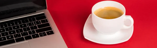 Vue panoramique de l'ordinateur portable avec écran vierge et tasse de café sur fond rouge — Photo de stock