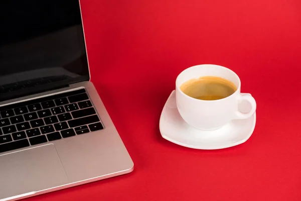 Laptop with blank screen and coffee cup on saucer on red background — Stock Photo