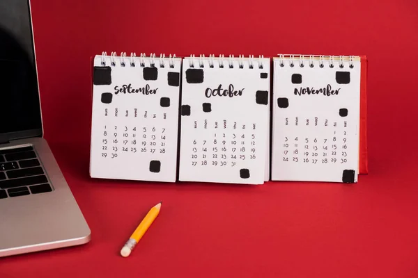 Laptop und Herbstmonate auf Kalender mit Bleistift auf rotem Hintergrund — Stockfoto