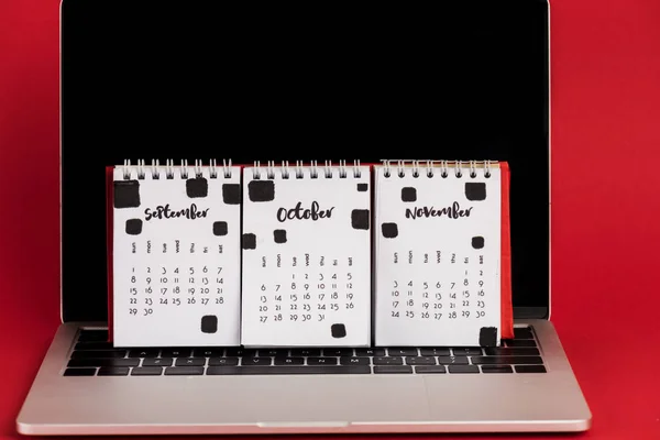 Calendario con i mesi autunnali sul computer portatile con schermo bianco su sfondo rosso — Foto stock