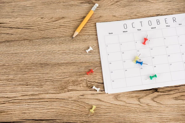 Vista superior de lápiz, alfileres de oficina y calendario de octubre sobre superficie de madera - foto de stock