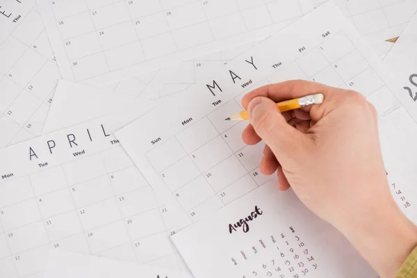 Vista recortada del hombre sosteniendo lápiz sobre calendarios mensuales - foto de stock