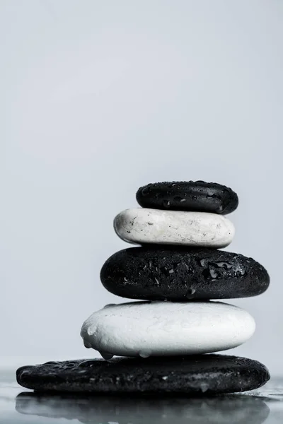 Vista de cerca de piedras zen apiladas en blanco y negro sobre vidrio húmedo aislado en gris - foto de stock