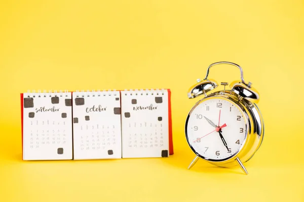 Reloj despertador y calendario con meses otoñales sobre fondo amarillo - foto de stock