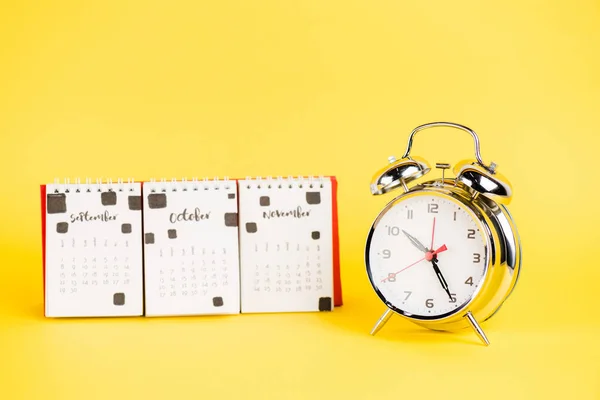 Reloj despertador y calendario con meses otoñales sobre fondo amarillo — Stock Photo