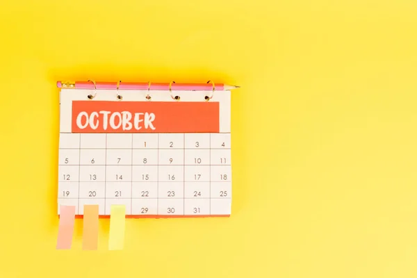 Vista dall'alto della matita, calendario con mese di ottobre e note appiccicose su sfondo giallo — Foto stock