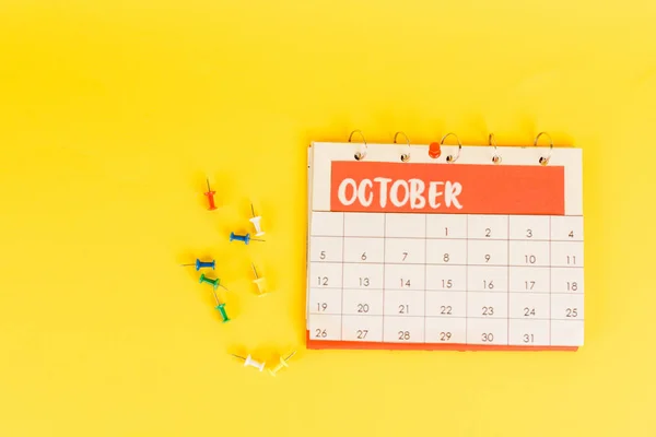 Vista superior do calendário com mês de outubro e pinos de escritório no fundo amarelo — Fotografia de Stock