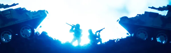 Escena de batalla con guerreros de juguete y tanques con iluminación sobre fondo azul, plano panorámico - foto de stock