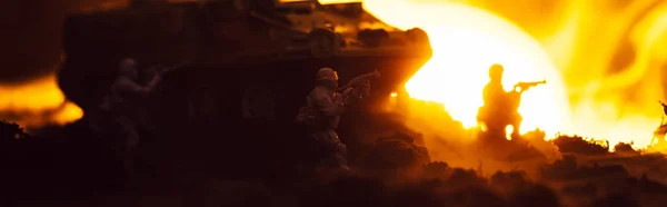 Escena de batalla con guerreros de juguete, tanque y fuego con puesta de sol al fondo, plano panorámico - foto de stock