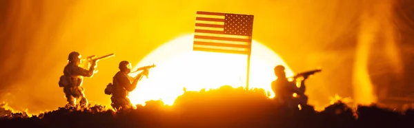 Escena de batalla con guerreros de juguete cerca de bandera americana en humo con puesta de sol en el fondo, tiro panorámico - foto de stock