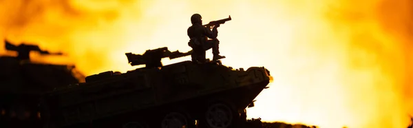 Kampfszene mit Silhouette eines Spielzeugsoldaten auf Panzer mit Feuer im Hintergrund, Panoramaaufnahme — Stockfoto