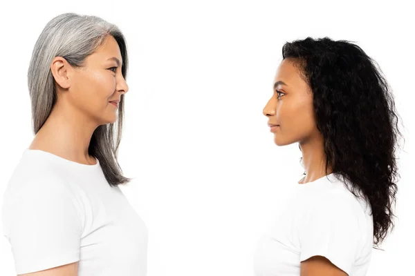 Seitenansicht glücklicher afrikanisch-amerikanischer und asiatischer Frauen, die sich isoliert auf weiß betrachten — Stockfoto