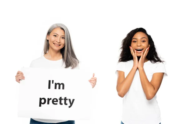 Happy african american and asian women near i`m pretty placard isolated on white — Stock Photo