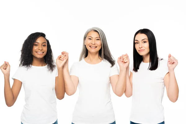 Heureuses femmes multiculturelles regardant la caméra et tenant les mains isolées sur blanc — Photo de stock