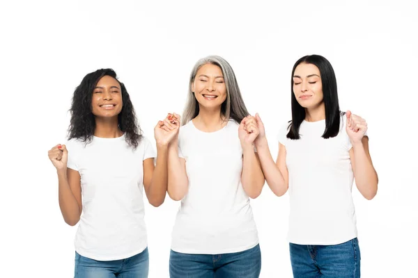 Lächelnde multikulturelle Frauen mit geschlossenen Augen, die die Hände isoliert auf Weiß halten — Stockfoto