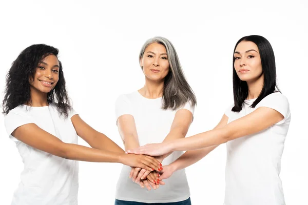 Alegres mujeres multiculturales poniendo las manos juntas aisladas en blanco - foto de stock