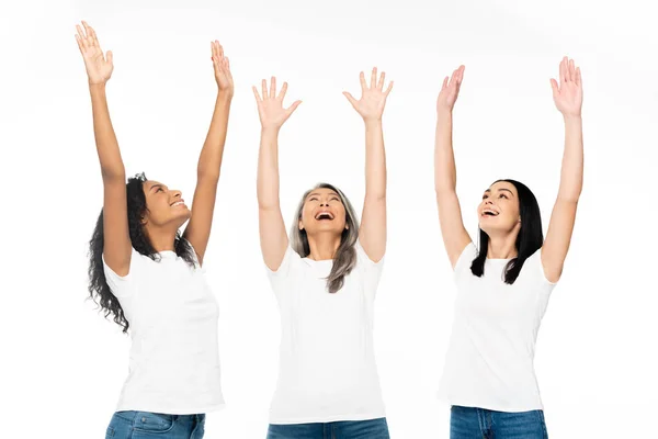 Mujeres multiculturales felices con las manos por encima de la cabeza mirando hacia arriba aislado en blanco - foto de stock