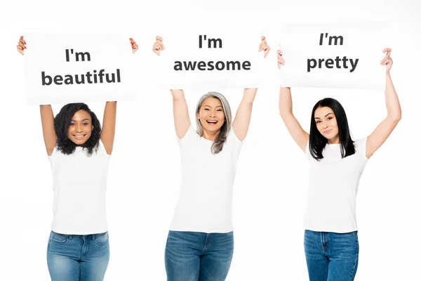 Happy multicultural women holding posters with lettering above head isolated on white — Stock Photo