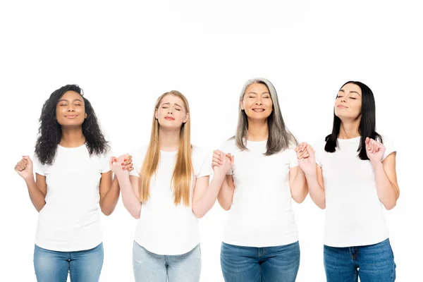 Glückliche multikulturelle Frauen mit geschlossenen Augen, die die Hände isoliert auf Weiß halten — Stockfoto