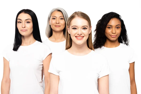 Четыре счастливые мультикультурные женщины в белых футболках, смотрящие в камеру, изолированную на белом — стоковое фото