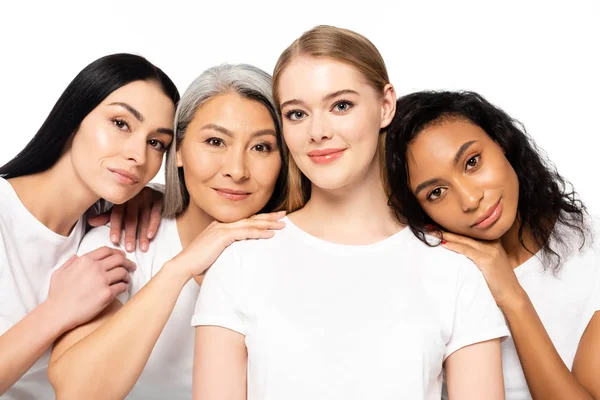 Cheerful multicultural women in white t-shirts looking at camera isolated on white — Stock Photo