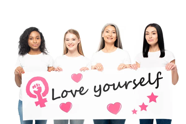 Mulheres multiculturais sorridentes segurando cartaz com amor-se lettering isolado no branco — Fotografia de Stock