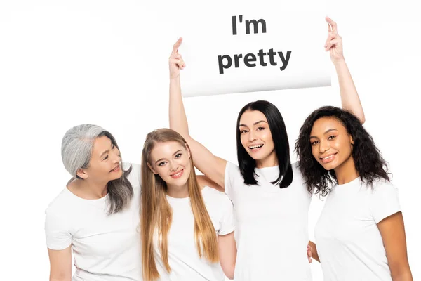 Happy multicultural women near placard with i`m pretty lettering isolated on white — Stock Photo