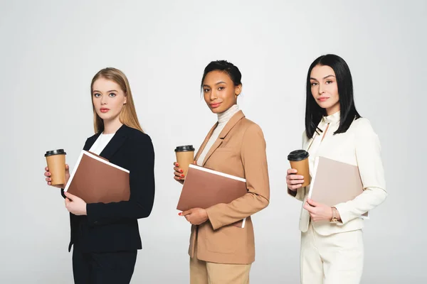 Multicultural businesswomen holding disposable cups and folders isolated on white — Stock Photo