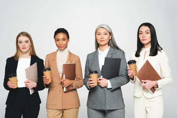 Cuatro empresarias multiculturales sosteniendo carpetas y vasos de papel aislados en blanco - foto de stock