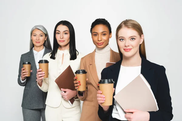 Vier fröhliche und multikulturelle Geschäftsfrauen mit Ordnern und Pappbechern auf weißem Grund — Stockfoto