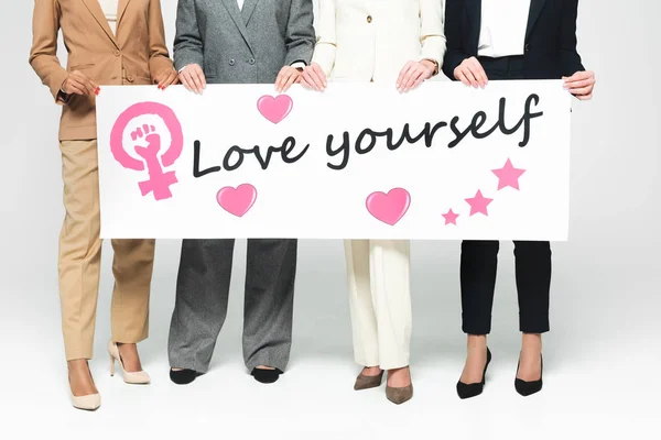 Cropped view of multicultural businesswomen holding placard with love yourself lettering on white — Stock Photo