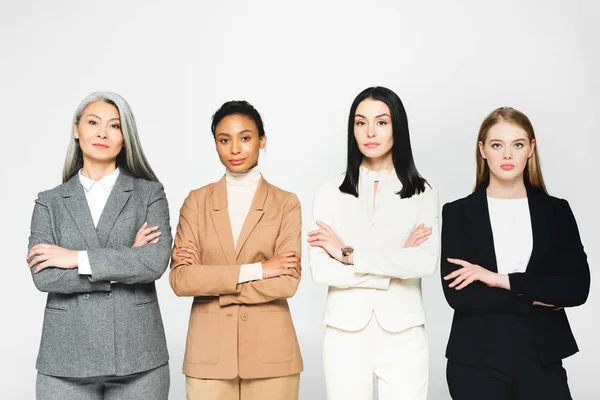 Multicultural businesswomen in suits standing with crossed arms isolated on white — Stock Photo