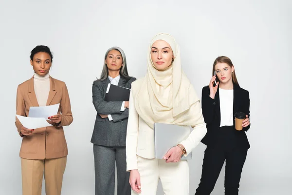 Mulheres de negócios multiculturais atraentes perto de mulher árabe com laptop isolado em branco — Fotografia de Stock