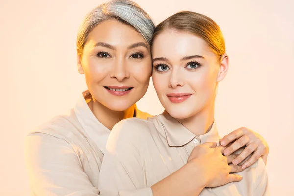 Duas mulheres multiculturais bonitas com maquiagem olhando para a câmera isolada no bege — Fotografia de Stock
