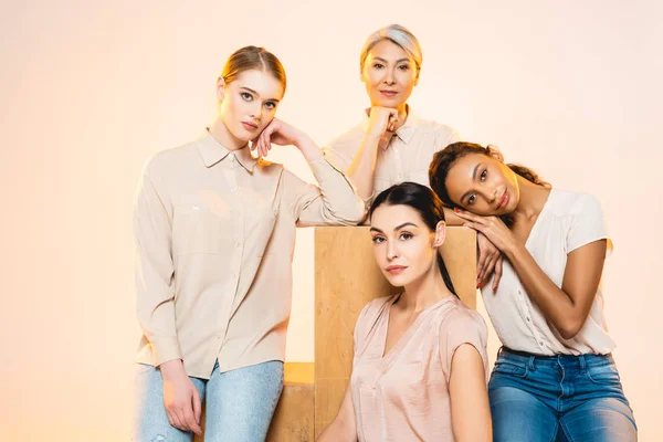 Schöne multikulturelle Frauen mit Make-up, die isoliert auf beige in die Kamera schauen — Stockfoto
