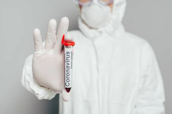 Foyer sélectif de l'épidémiologiste en combinaison Hazmat montrant tube à essai avec échantillon de sang sur fond gris — Photo de stock