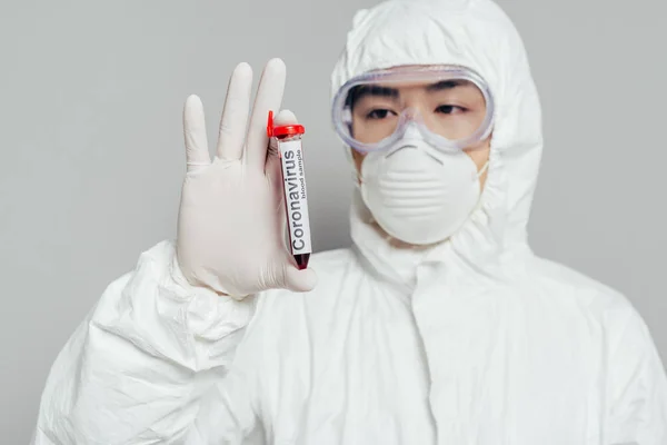 Épidémiologiste asiatique en combinaison Hazmat et masque respirateur montrant éprouvette avec échantillon de sang sur fond gris — Photo de stock