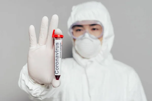 Selektiver Fokus des asiatischen Epidemiologen in Schutzanzug und Atemmaske mit Reagenzglas mit Blutprobe auf grauem Hintergrund — Stockfoto