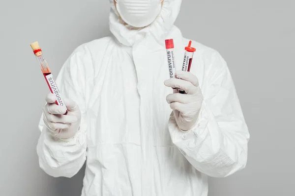 Visão parcial do epidemiologista em tubos de ensaio de retenção de fatos de protecção contra riscos com amostras de sangue sobre fundo cinzento — Fotografia de Stock