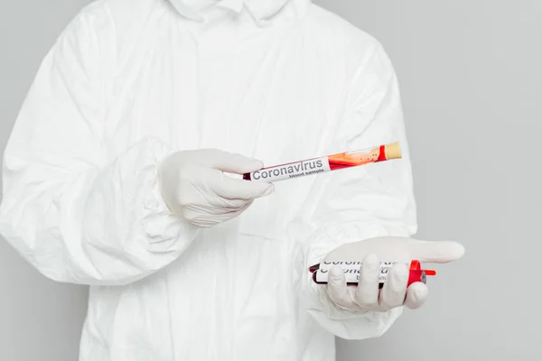 Cropped view of epidemiologist in hazmat suit holding test tubes with blood samples isolated on grey — Stock Photo